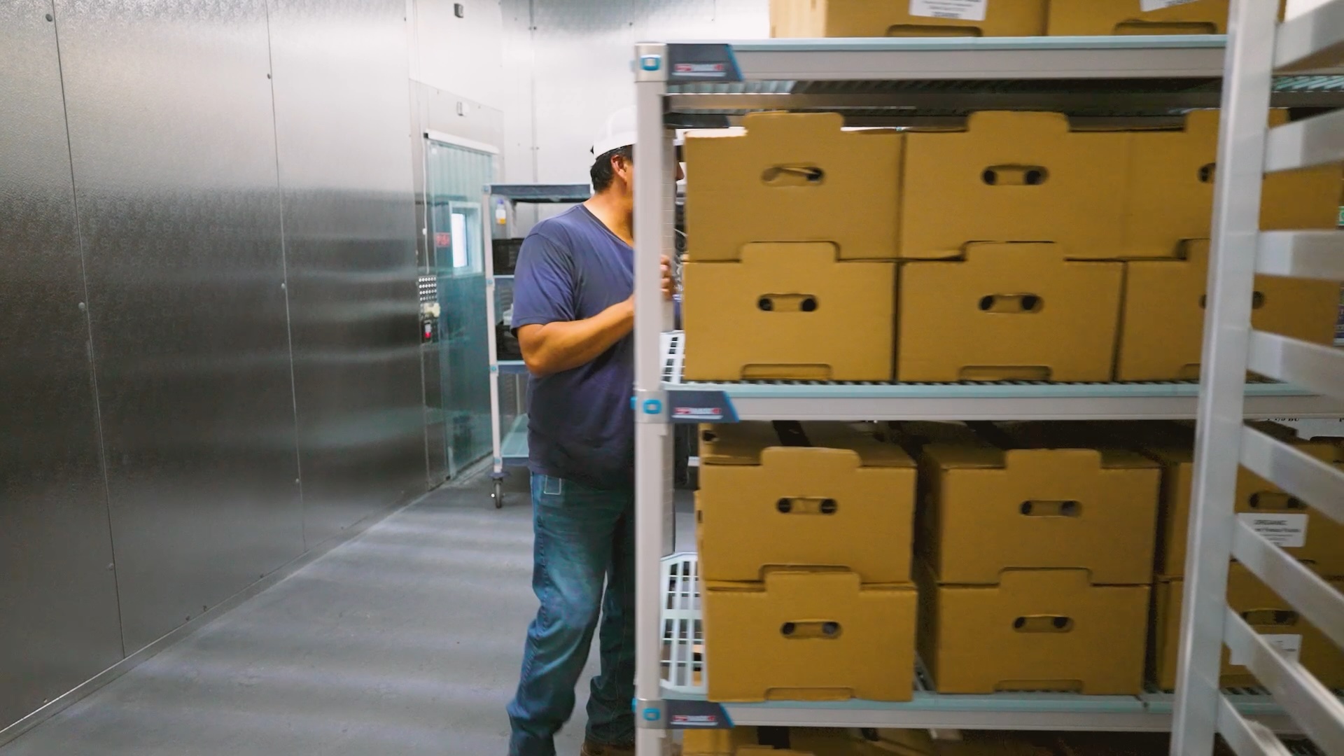 A worker moves boxes of fresh produce in a walk in cold storage room